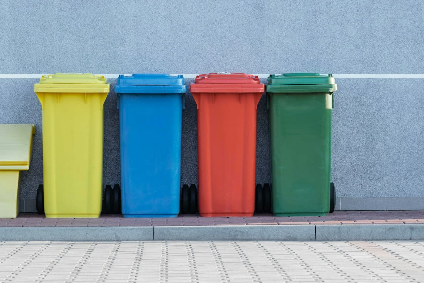 Four color-coded waste bins beside a pavement